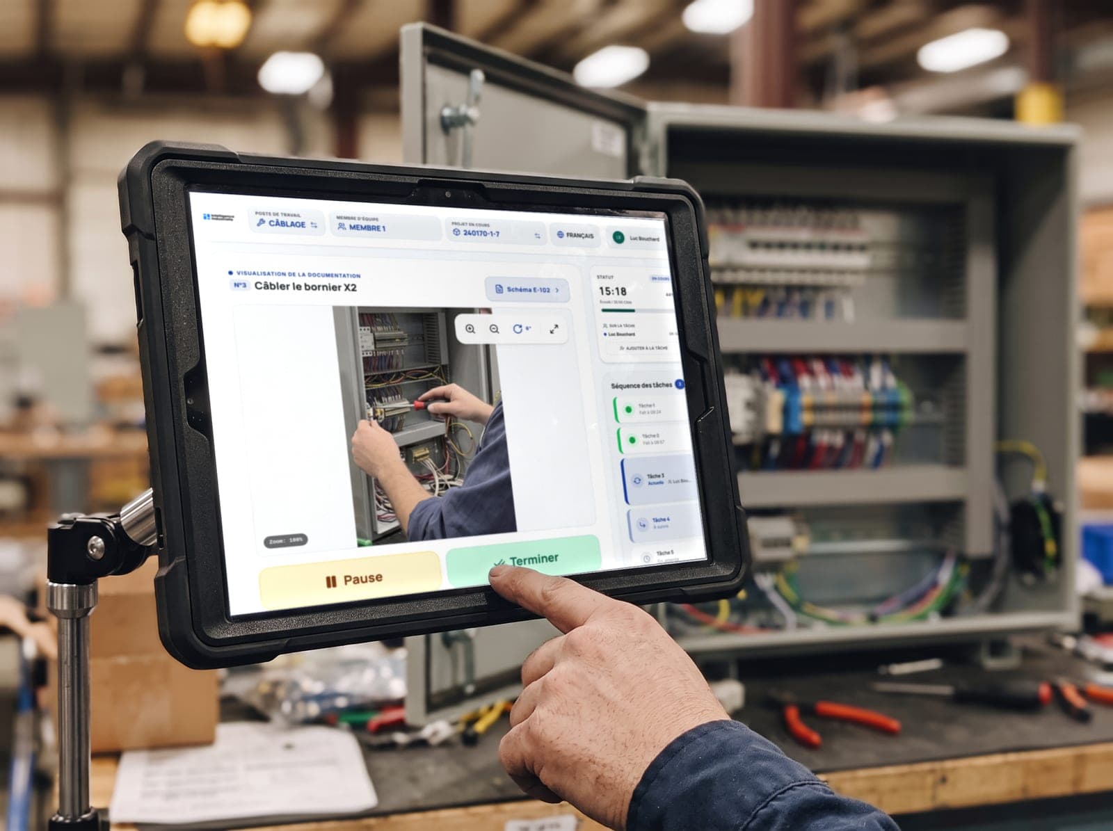 Opérateur qui termine une tâche de câblage sur la tablette CLOCK, devant une armoire électrique